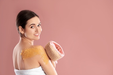 Young woman applying natural scrub on her shoulder against color background