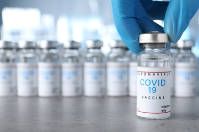 Photo of Doctor taking glass vial with COVID-19 vaccine from table, closeup. Space for text