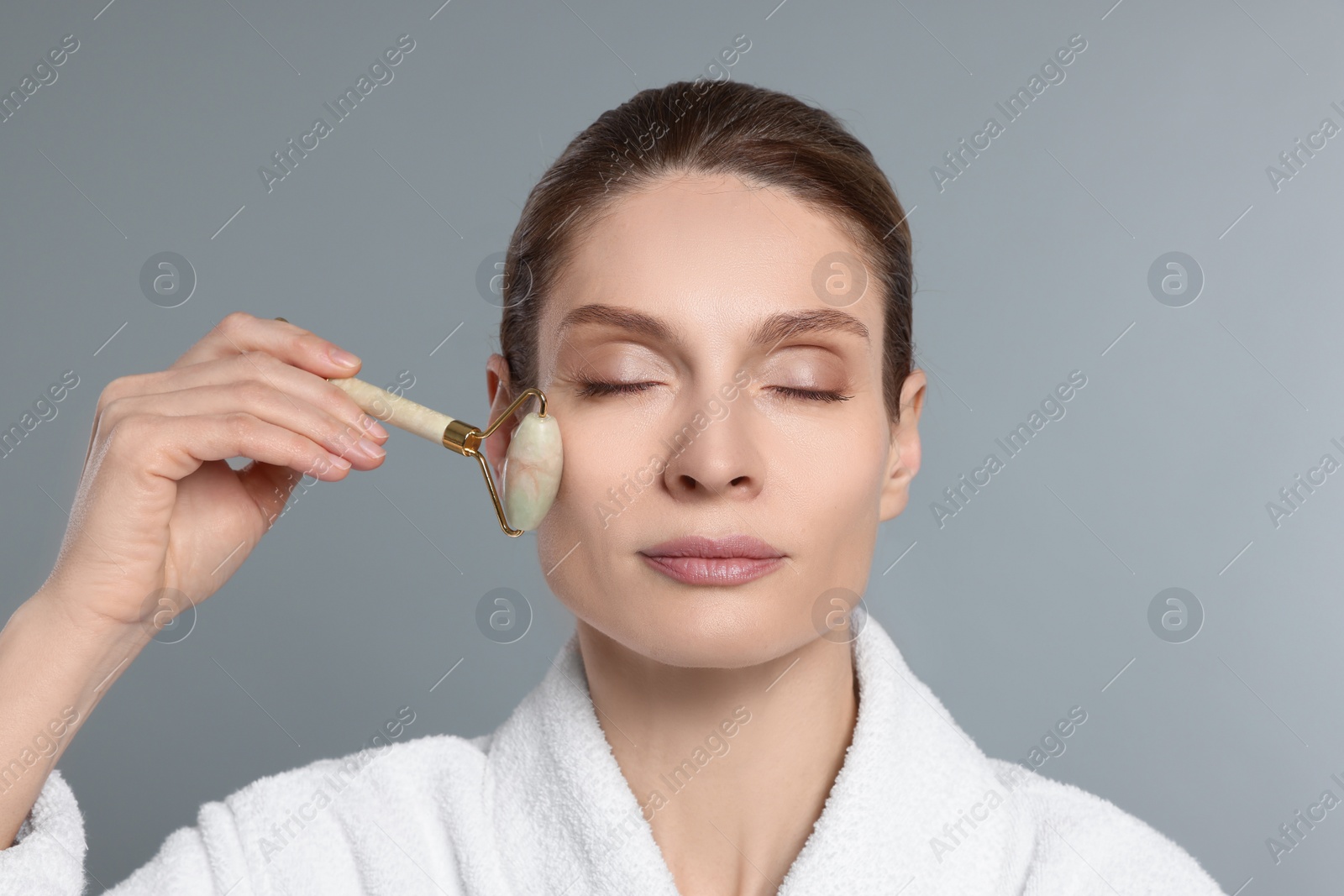 Photo of Woman massaging her face with jade roller on grey background