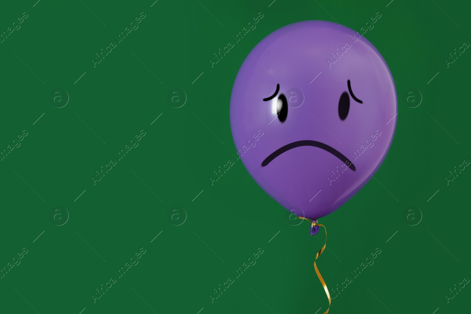 Image of Purple balloon with sad face on green background. Space for text