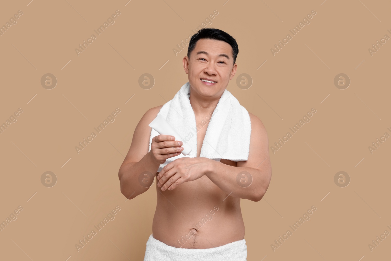 Photo of Man applying body cream onto his hand against light brown background