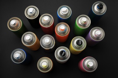 Photo of Cans of different graffiti spray paints on black background, flat lay