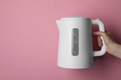 Woman holding modern electric kettle on pink background, closeup. Space for text