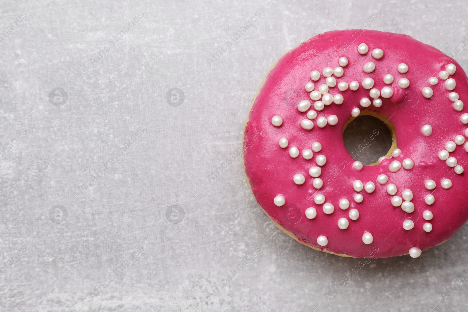 Photo of Tasty glazed donut decorated with sprinkles on light grey table, closeup. Space for text