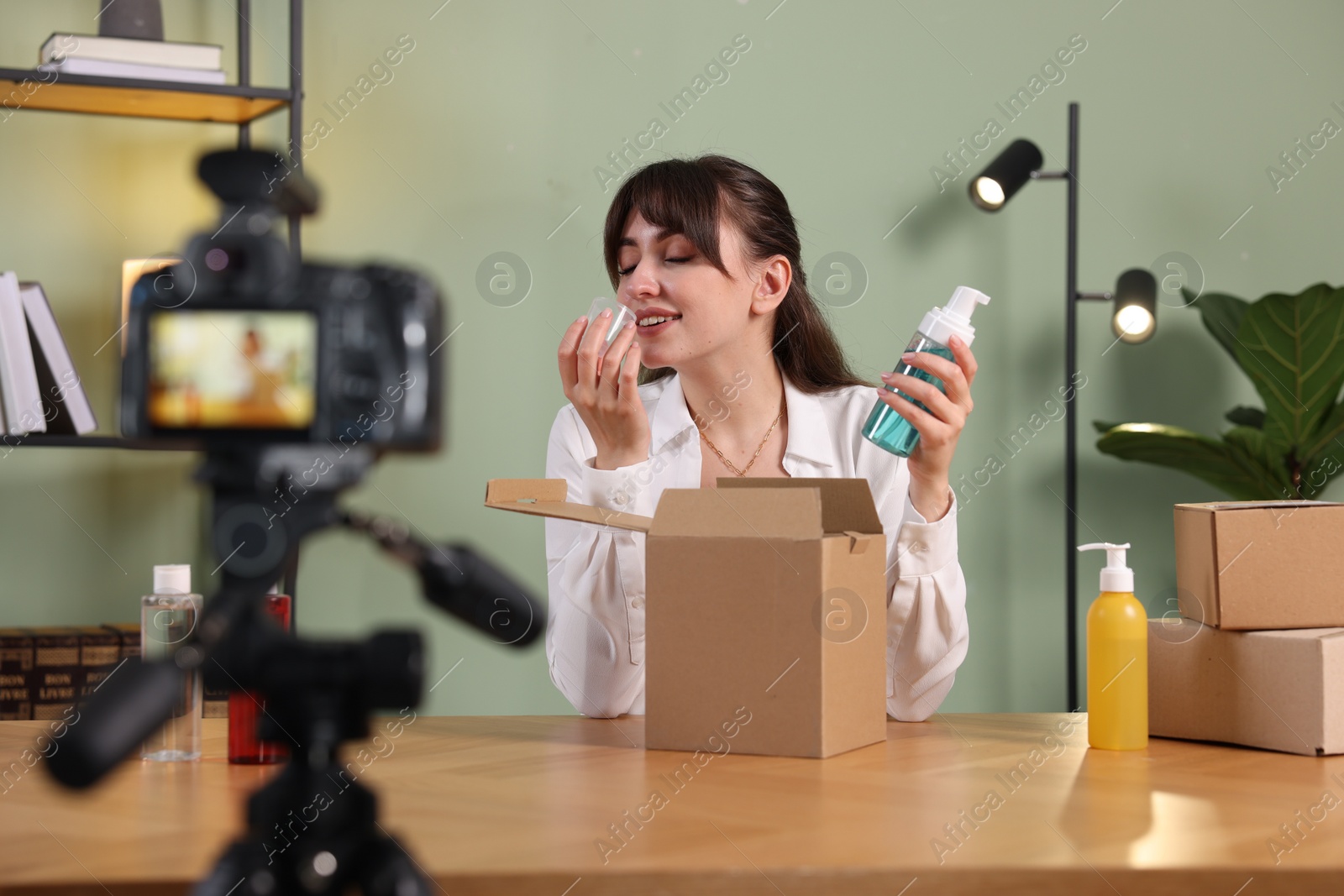 Photo of Smiling beauty blogger recording video while smelling cosmetic product at home
