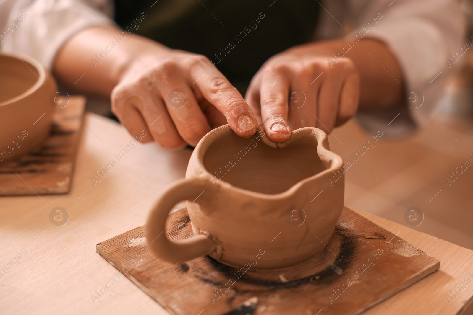 Photo of Pottery crafting. Woman sculpting with clay at table, closeup