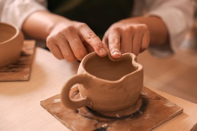 Photo of Pottery crafting. Woman sculpting with clay at table, closeup