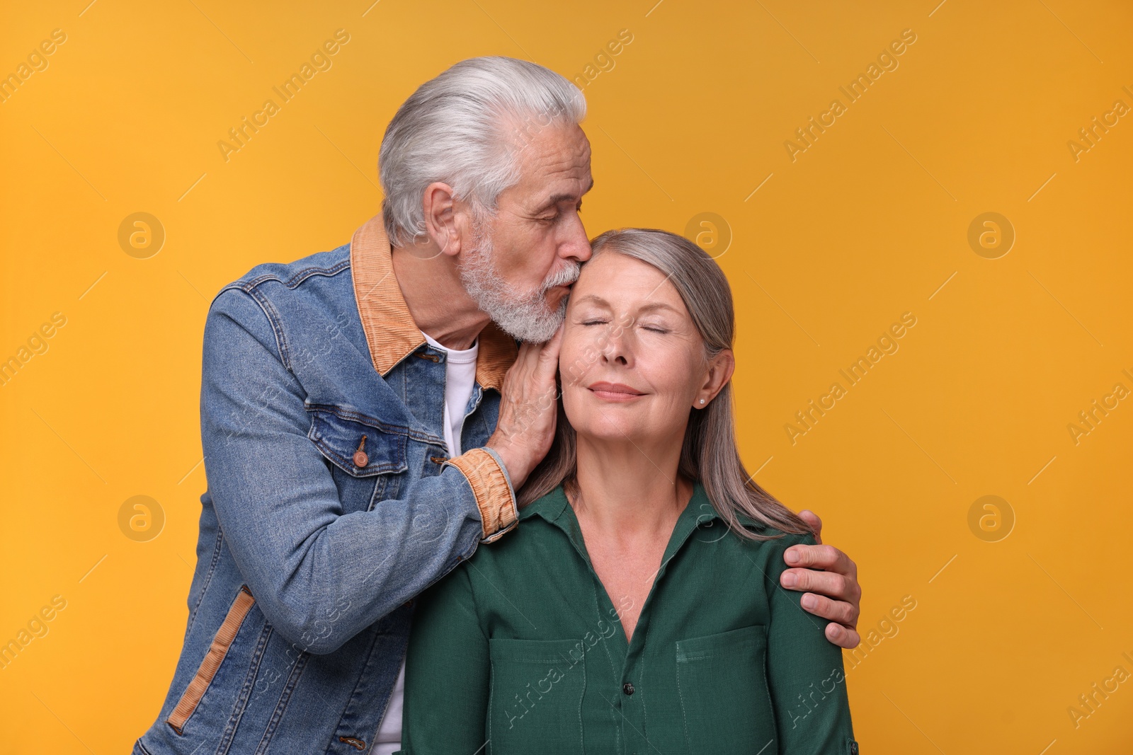 Photo of Senior man kissing his beloved woman on orange background