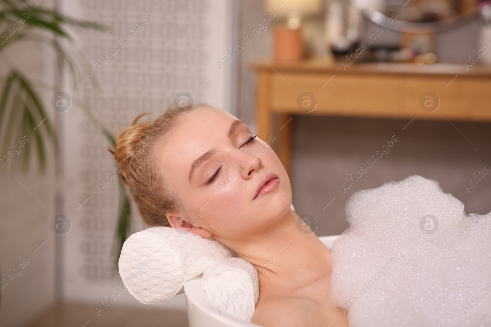 Photo of Young woman using pillow while enjoying bubble bath indoors