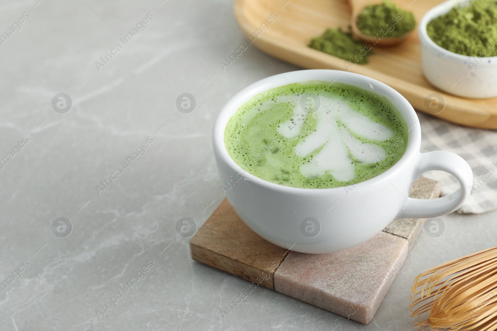 Photo of Cup of fresh matcha latte on light grey marble table, closeup. Space for text