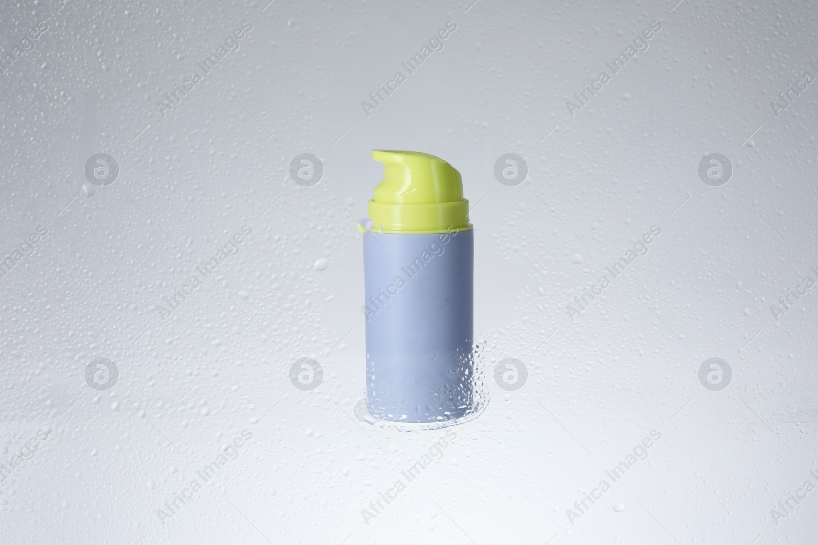 Photo of Bottle with moisturizing cream on light background, view through wet glass