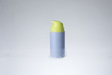 Bottle with moisturizing cream on light background, view through wet glass