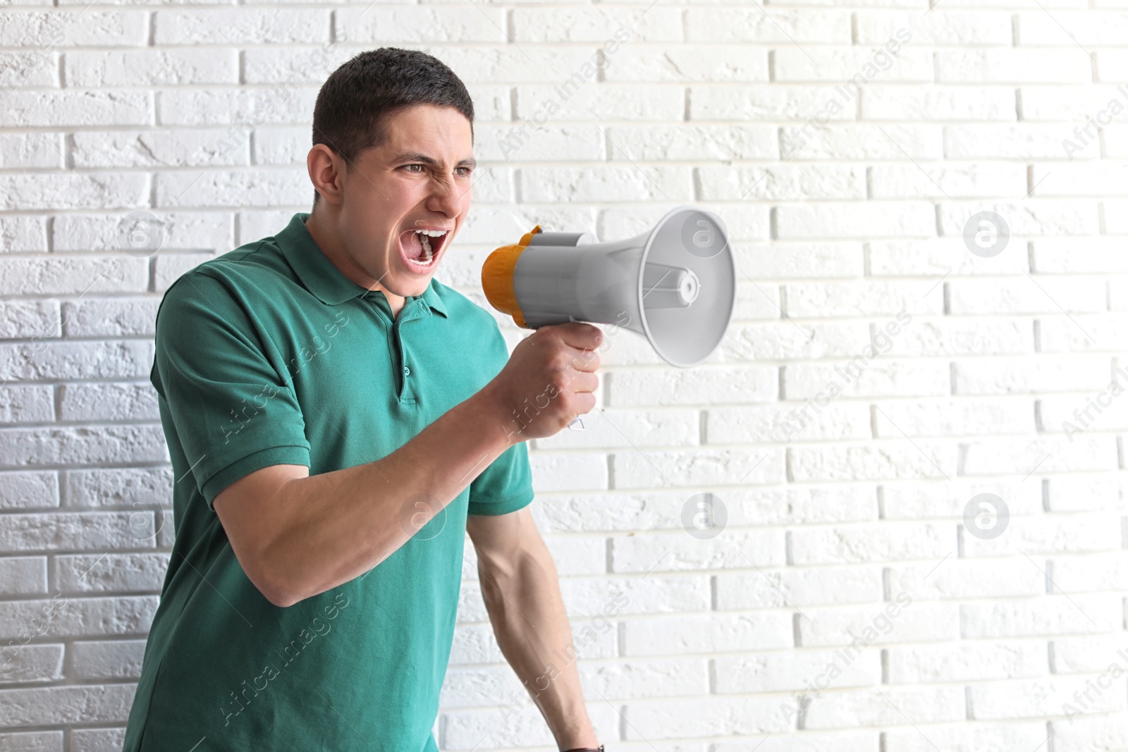 Photo of Portrait of young man using megaphone near brick wall. Space for text