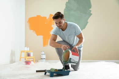 Photo of Young man pouring paint from bucket into tray indoors. Home repair