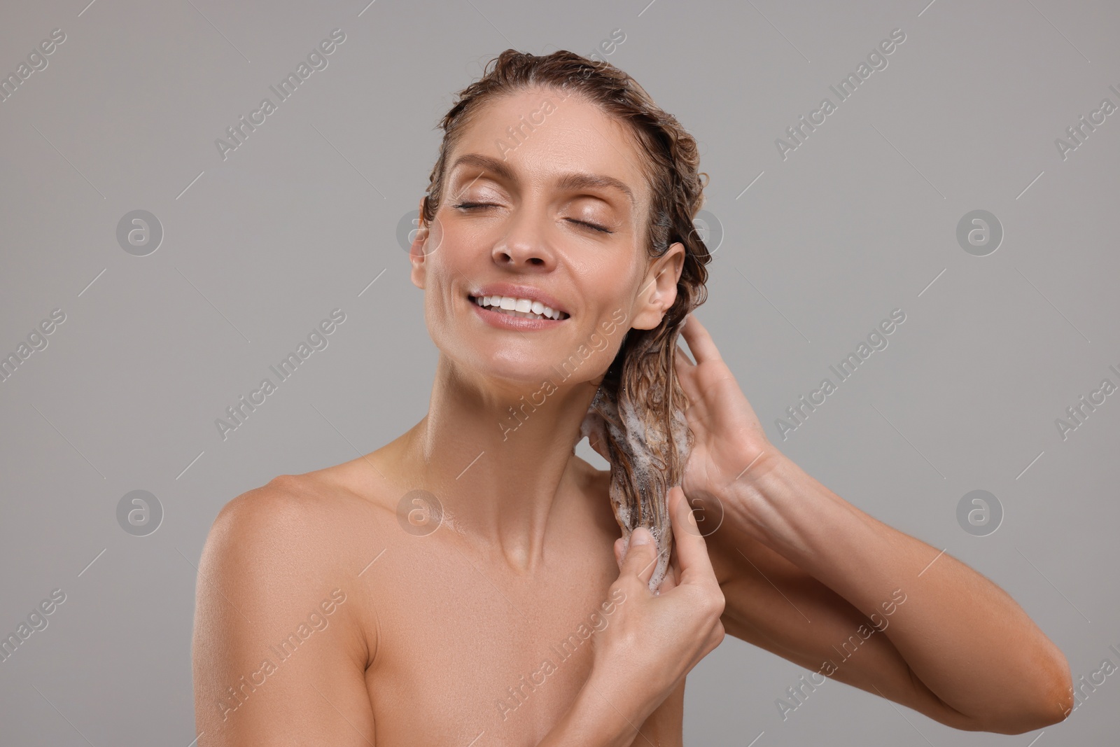 Photo of Portrait of beautiful happy woman washing hair on light grey background