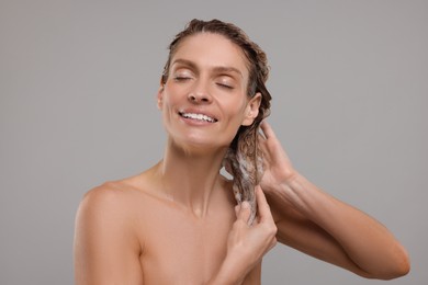 Photo of Portrait of beautiful happy woman washing hair on light grey background