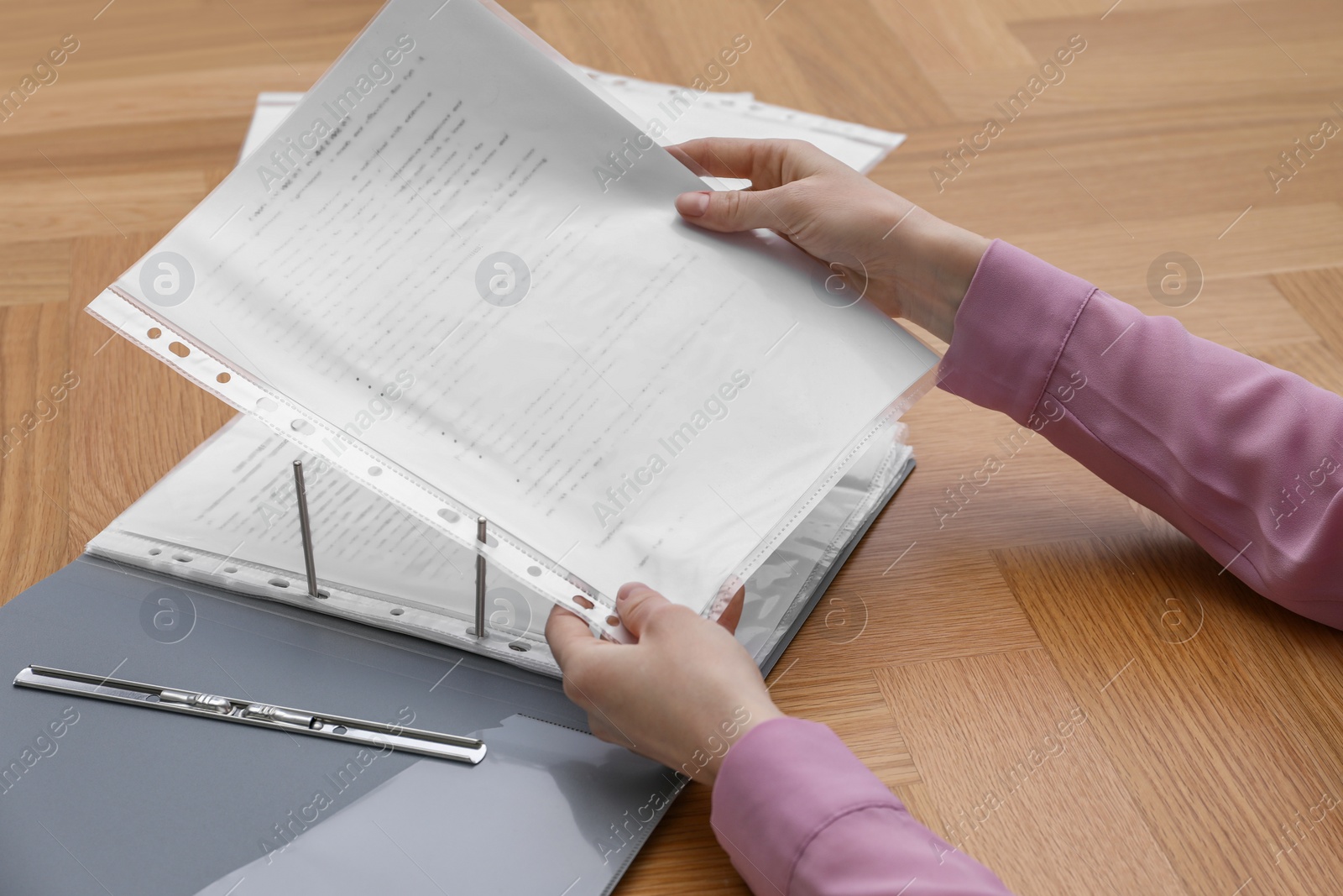 Photo of Woman putting punched pocket with document into folder at wooden table, closeup