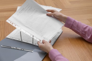 Woman putting punched pocket with document into folder at wooden table, closeup