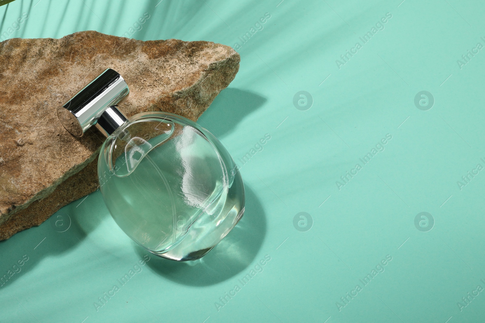Photo of Luxury perfume in bottle and stone on turquoise background, above view. Space for text