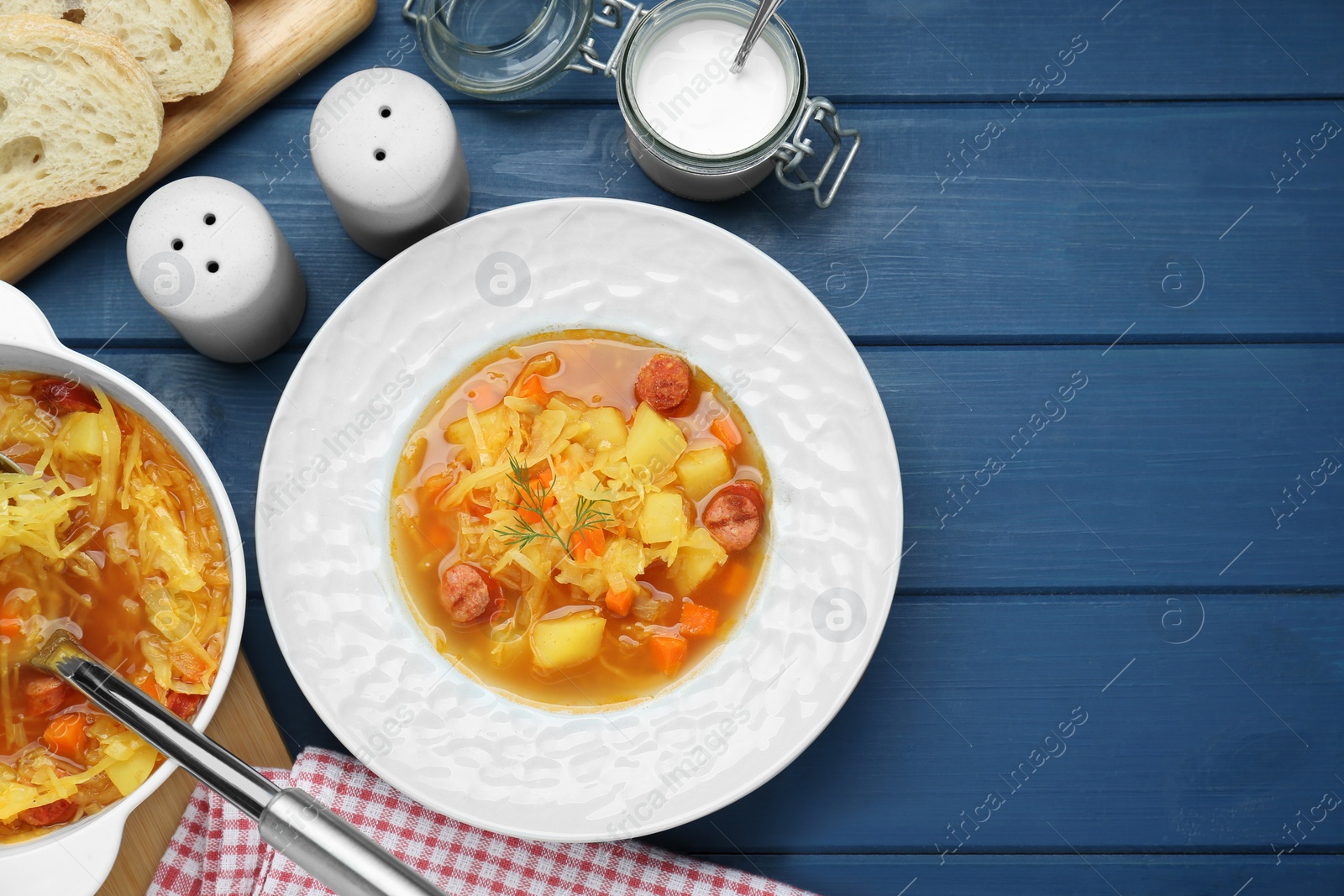 Photo of Delicious sauerkraut soup with smoked sausages served on blue wooden table, flat lay. Space for text