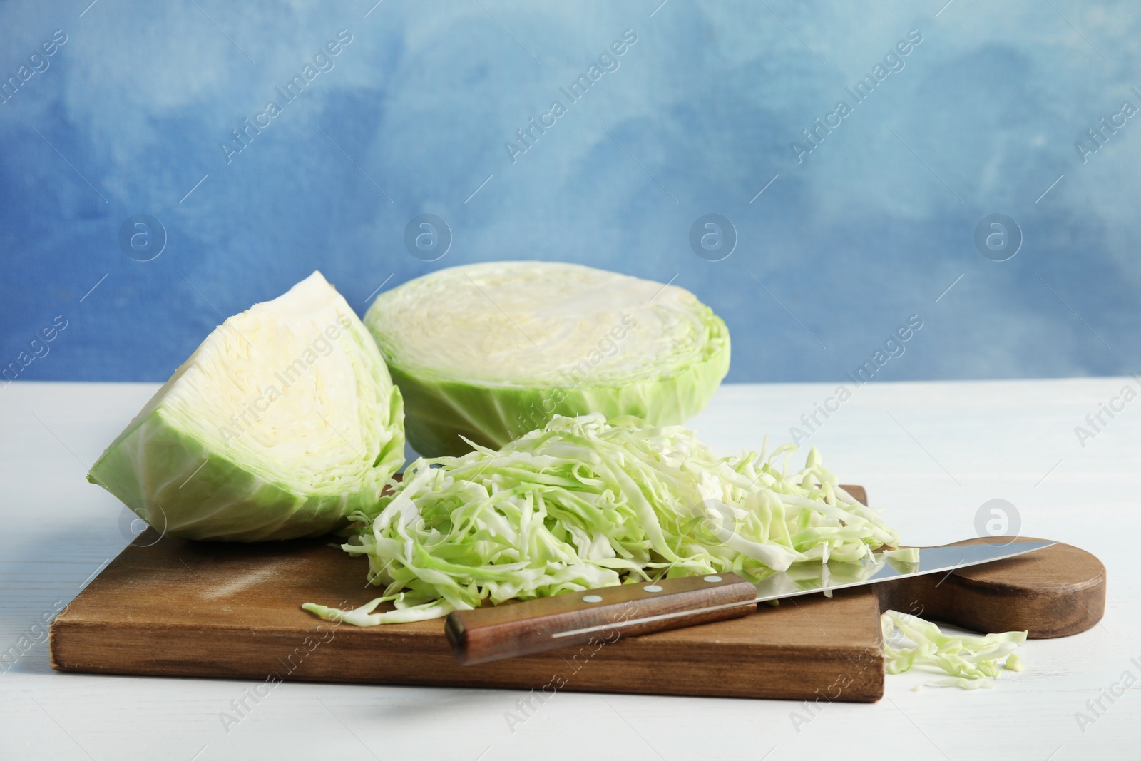 Photo of Cutting board with chopped and sliced cabbage on table