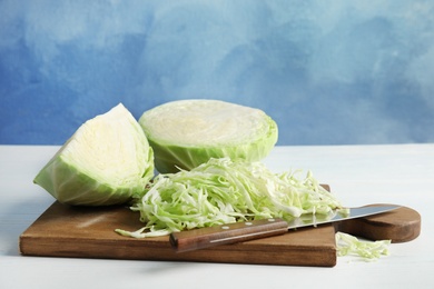 Photo of Cutting board with chopped and sliced cabbage on table