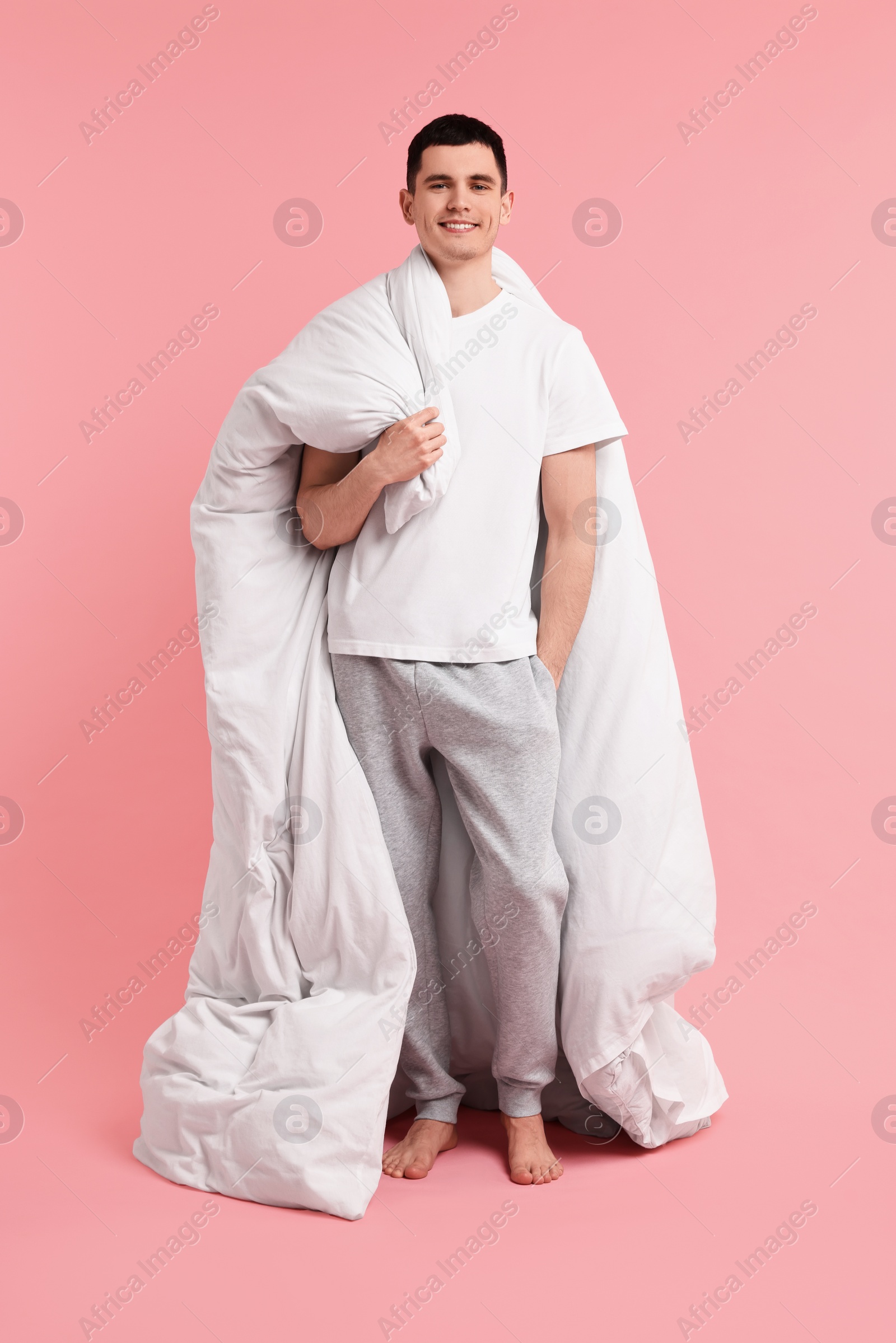 Photo of Happy man in pyjama holding blanket on pink background