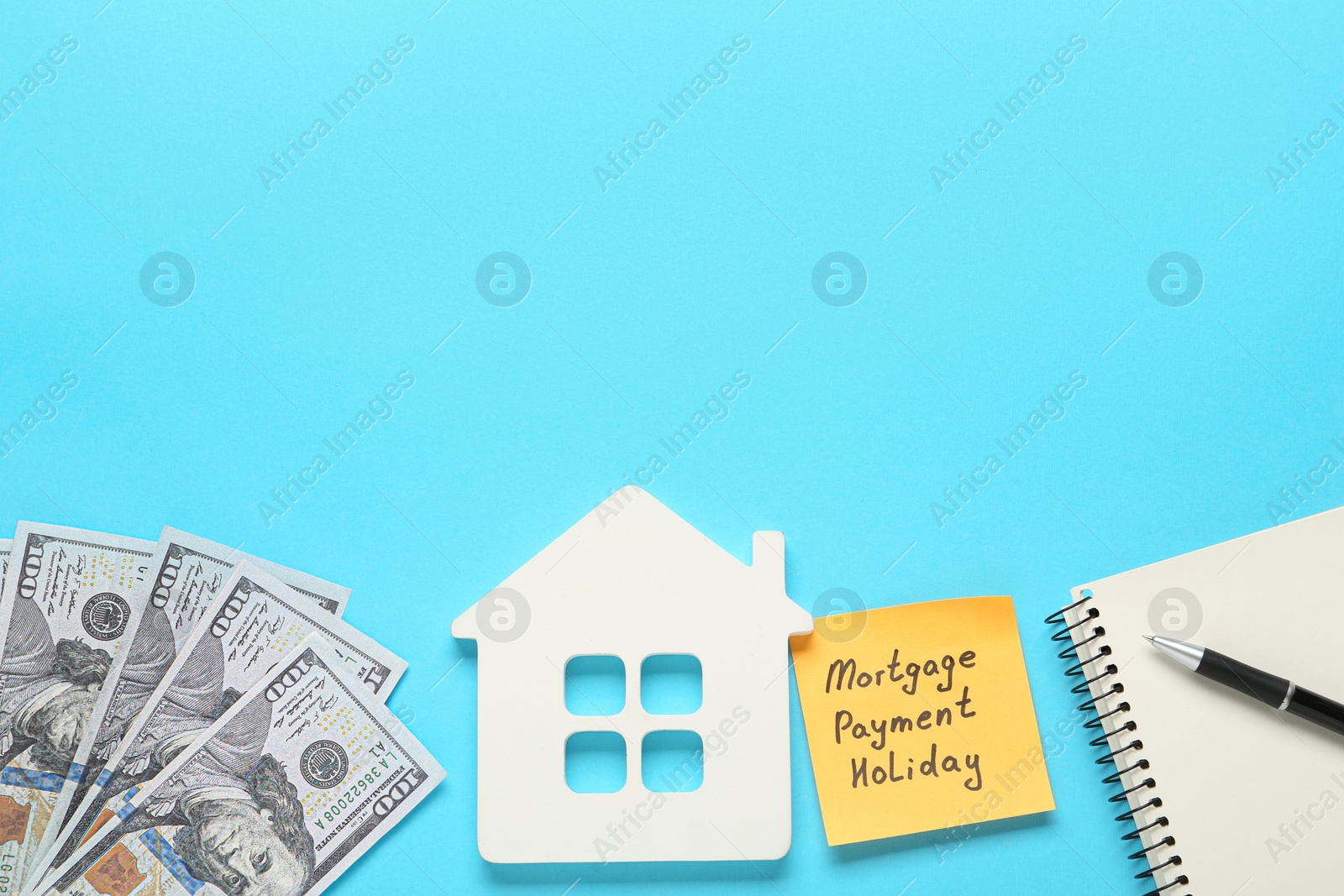 Photo of Note with words Mortgage Payment Holiday, house model, notebook and money on light blue background, flat lay. Space for text