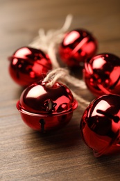 Photo of Shiny red sleigh bells on wooden table, closeup