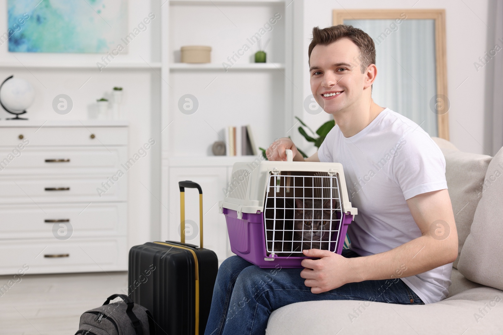Photo of Travel with pet. Man holding carrier with cute cat on sofa at home, space for text