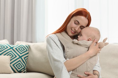 Photo of Mother with toy bunny holding her child in sling (baby carrier) at home