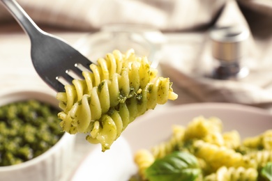 Photo of Fork with delicious basil pesto pasta over plate, closeup
