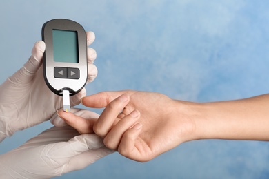 Doctor checking blood sugar level with glucometer on color background. Diabetes test