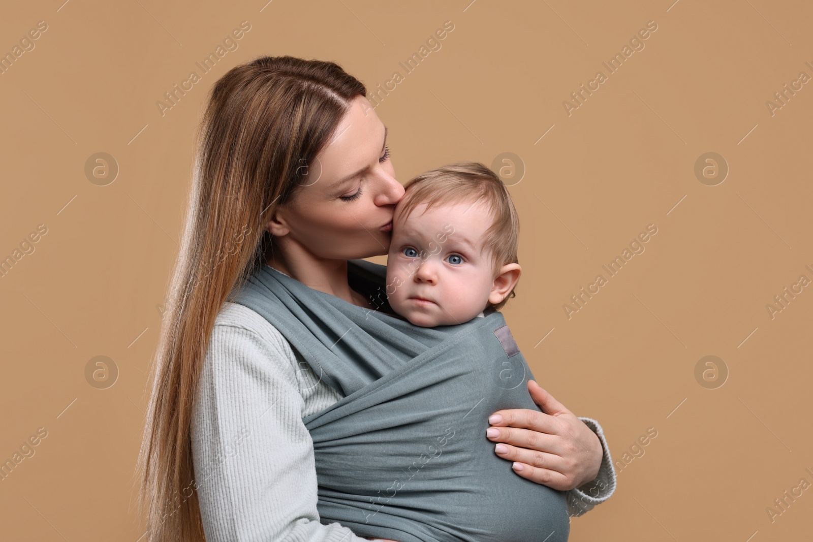 Photo of Mother holding her child in baby wrap on light brown background