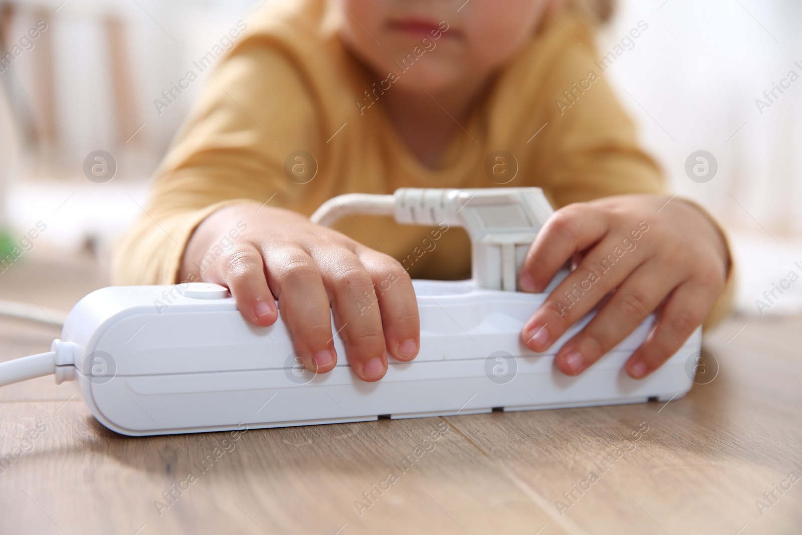 Photo of Little child playing with power strip and plug on floor indoors, closeup. Dangerous situation