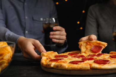 Friends taking tasty pepperoni pizza at table, closeup