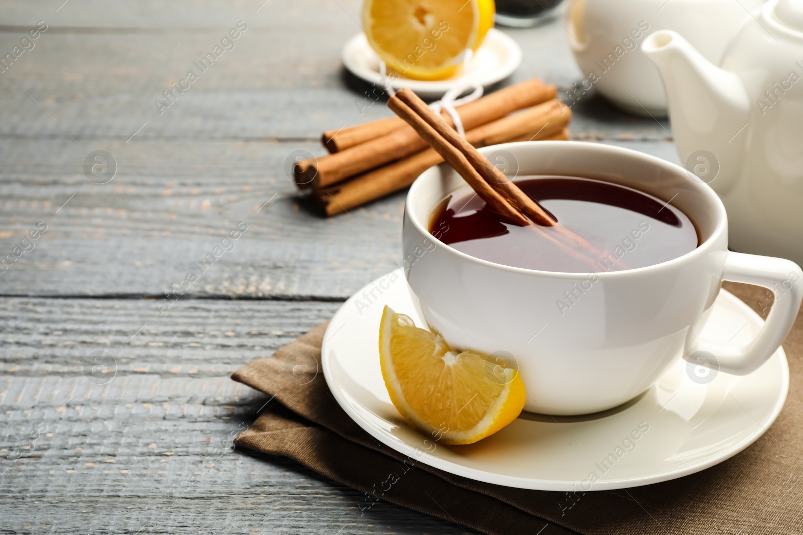 Photo of Delicious hot tea with cinnamon and lemon on grey wooden table. Space for text