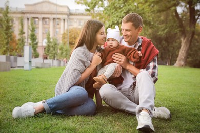 Photo of Happy parents with their adorable baby on green grass in park