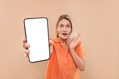 Photo of Surprised woman holding smartphone with blank screen on beige background