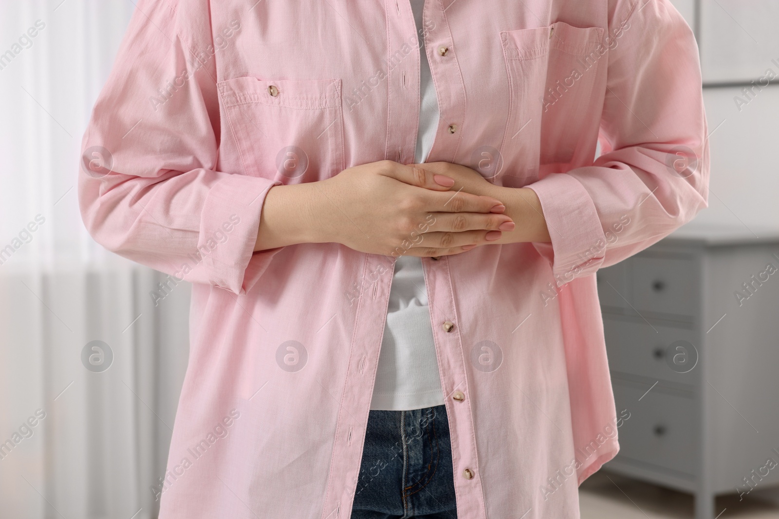 Photo of Young woman suffering from stomach pain at home, closeup