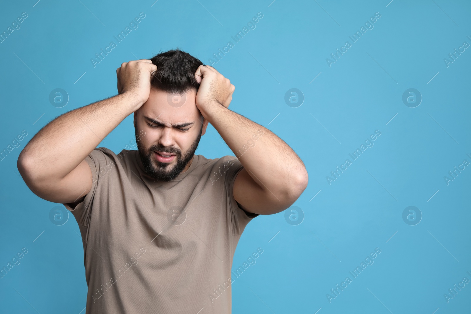 Photo of Young man suffering from headache on light blue background, space for text