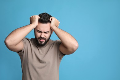 Photo of Young man suffering from headache on light blue background, space for text