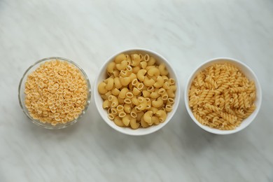 Photo of Different types of pasta on white marble table, flat lay