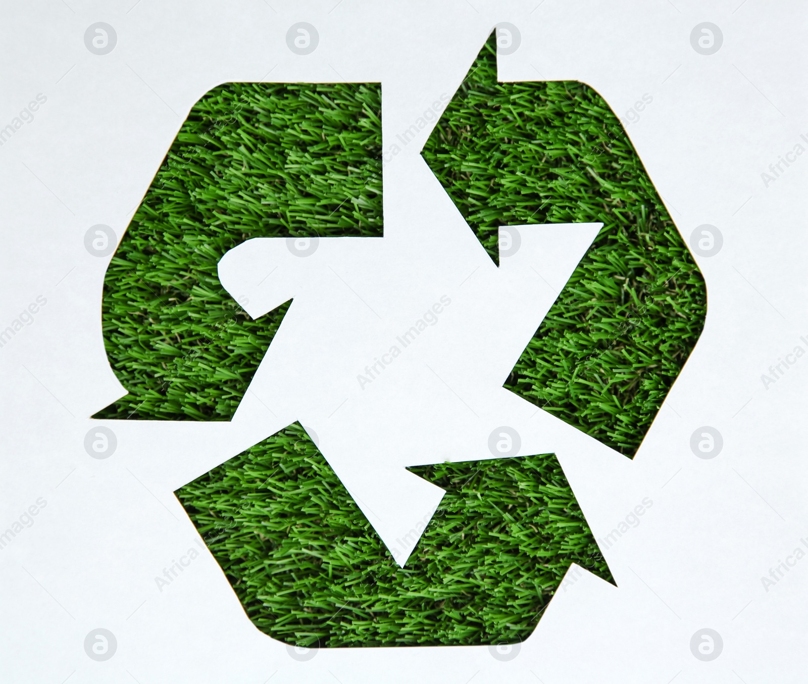 Photo of Sheet of paper with cutout recycling symbol on green grass, top view