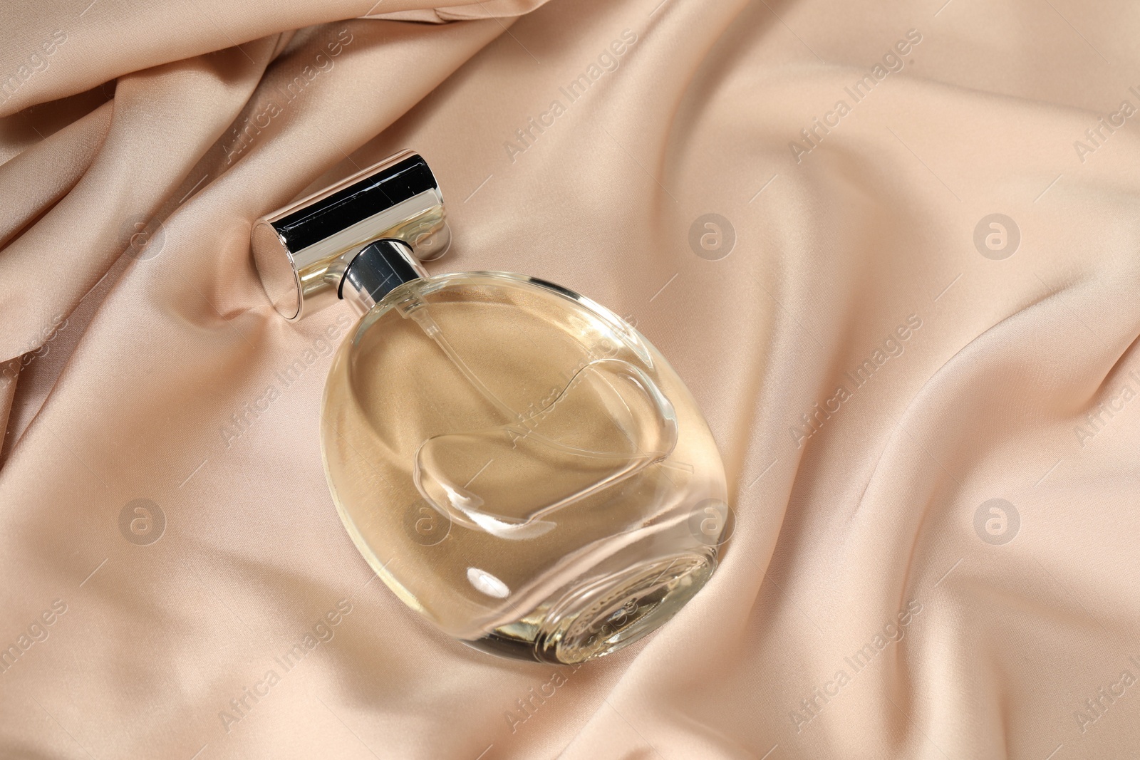 Photo of Luxury perfume in bottle on beige silk fabric