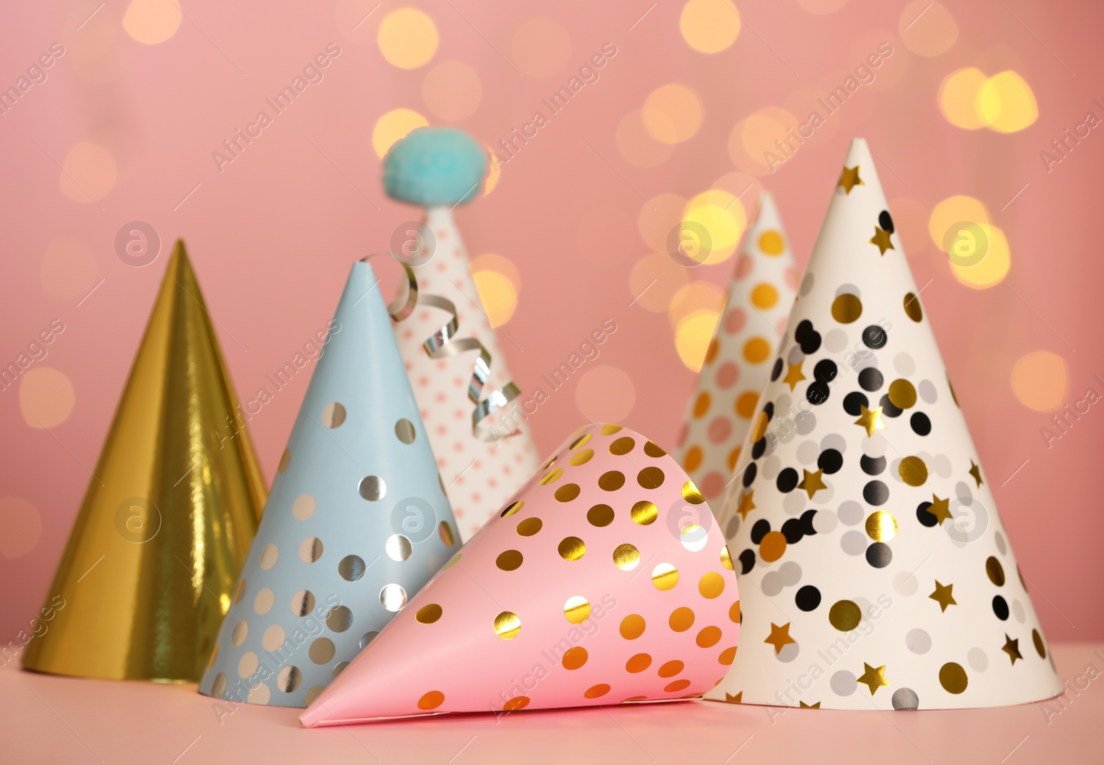 Photo of Beautiful party hats on pink table against blurred festive lights