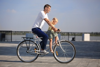 Father and daughter riding bicycle outdoors on sunny day