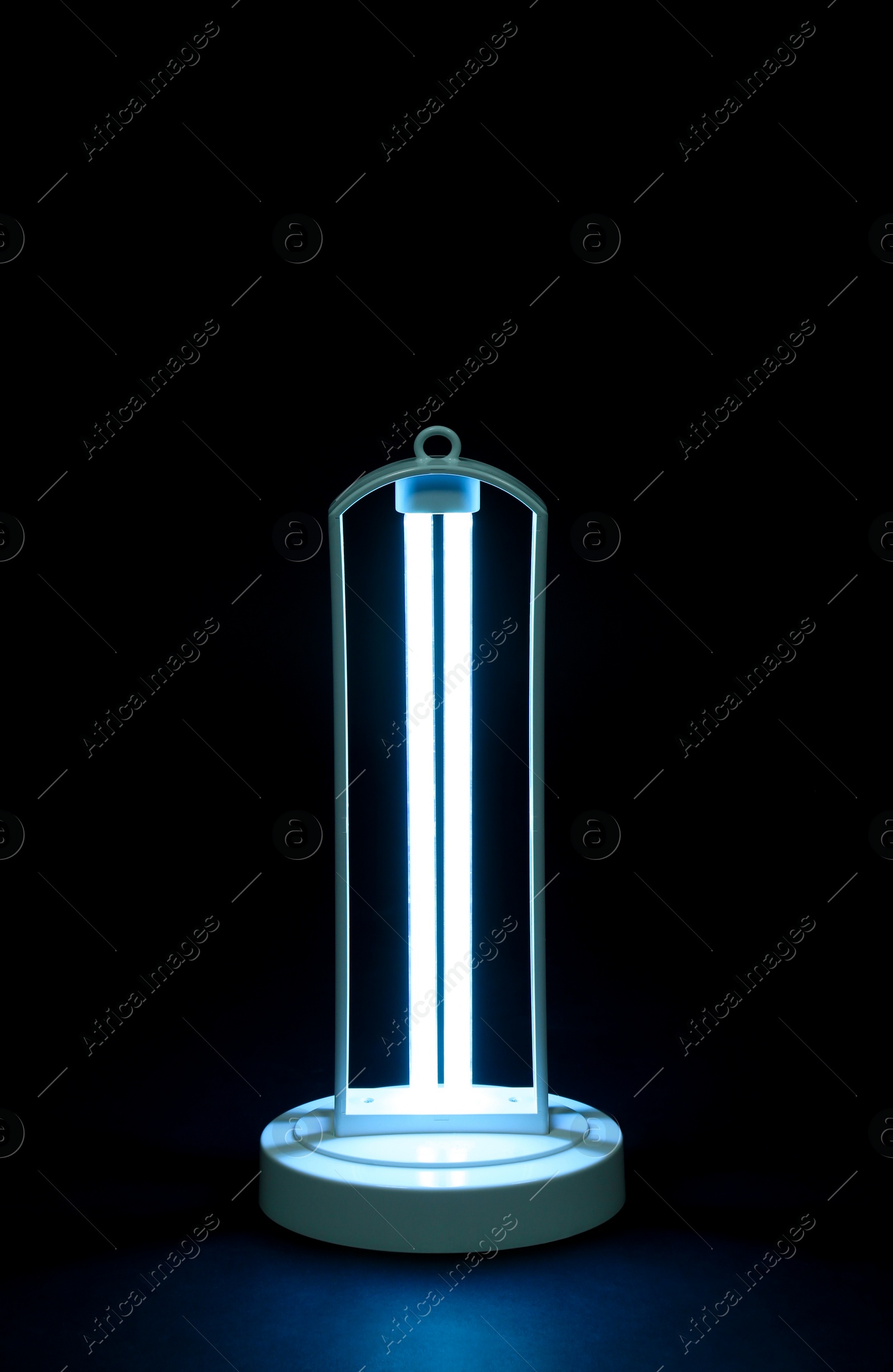 Photo of Modern ultraviolet lamp glowing on black background