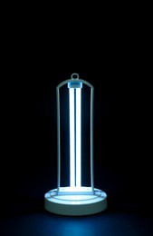 Photo of Modern ultraviolet lamp glowing on black background