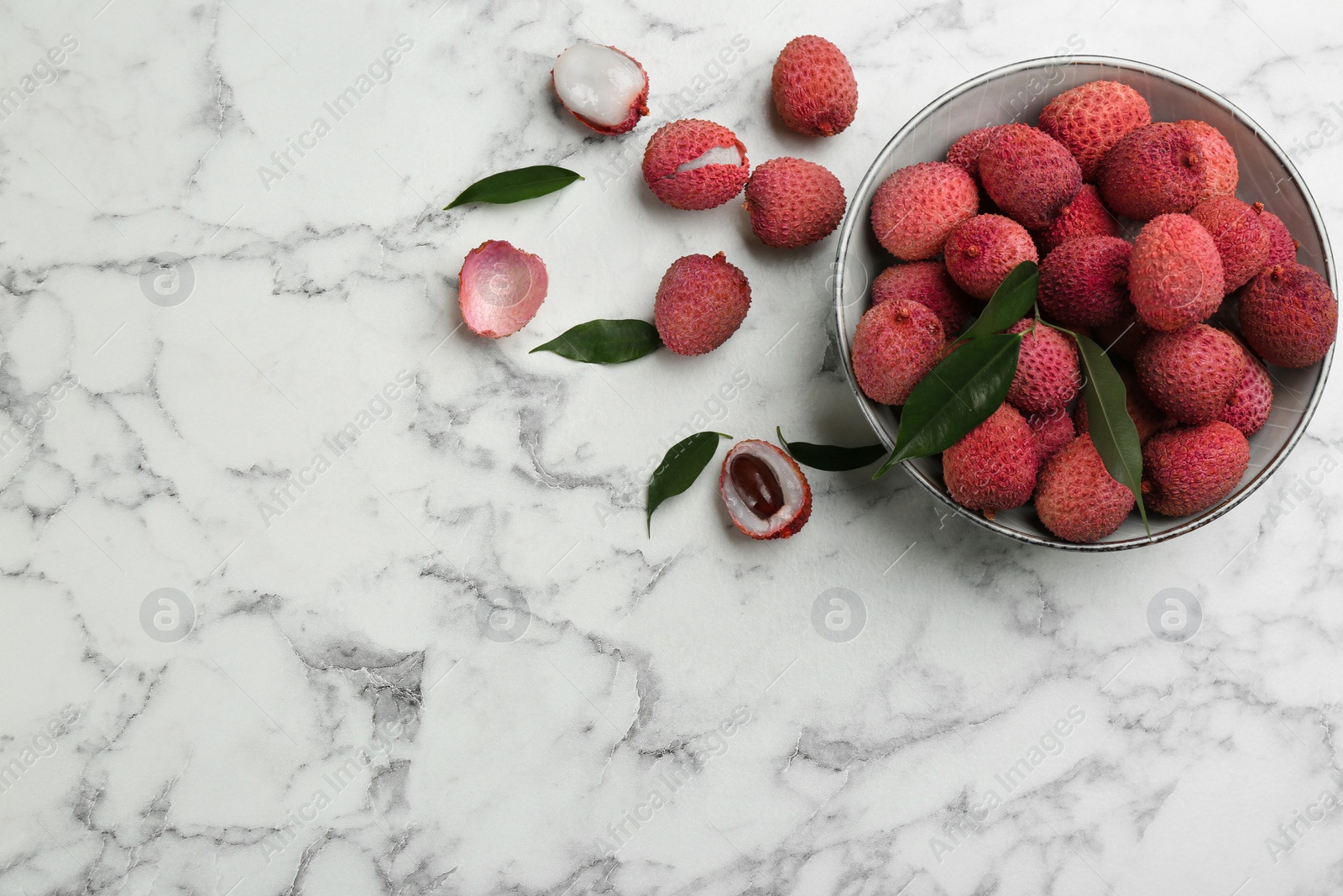 Photo of Fresh ripe lychee fruits in bowl on white marble table, flat lay. Space for text